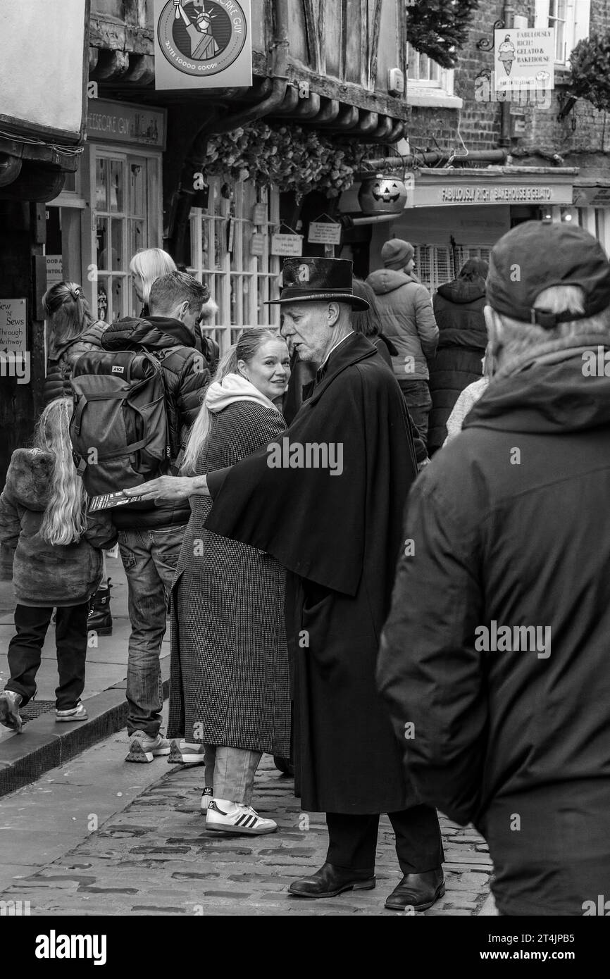 Flyers for the Ghost Walk are being distributed by an elderly gentleman dressed in full black and a bowler hat along The Shambles in York, UK. Stock Photo