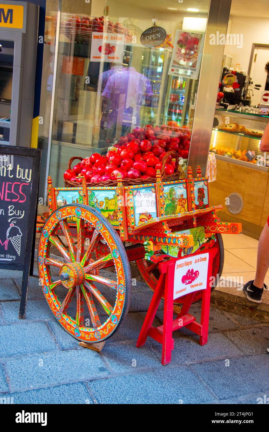 Sicily, Taormina, Italy - 28 September 2023. A brightly painted wooden cart with a basket of fresh pomegranates in front of a traditional fresh fruit Stock Photo