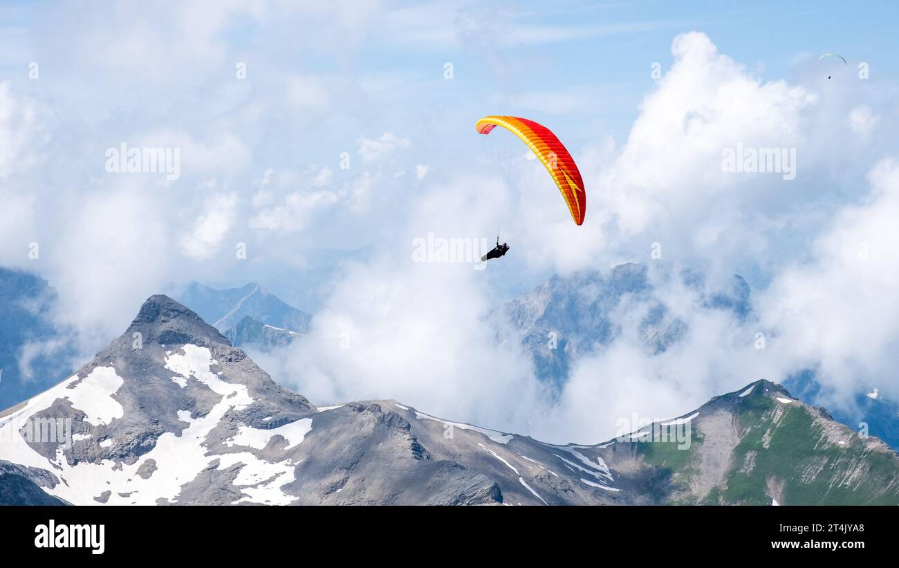 A paraglider in Swiss alps flys in front of snow covered mountains Stock Photo