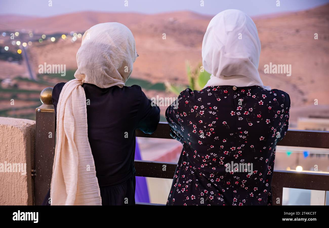 Two females wearing hijab and islamic wears having vacation in resort with smile on their face and beautiful blurred lights in the background Stock Photo