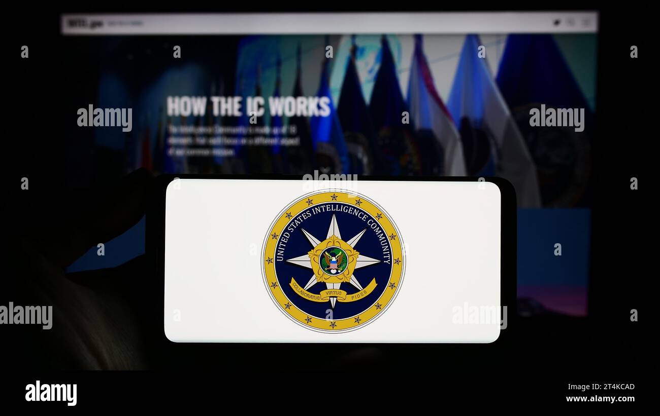 Person holding smartphone with seal of agency group United States Intelligence Community (IC) in front of website. Focus on phone display. Stock Photo