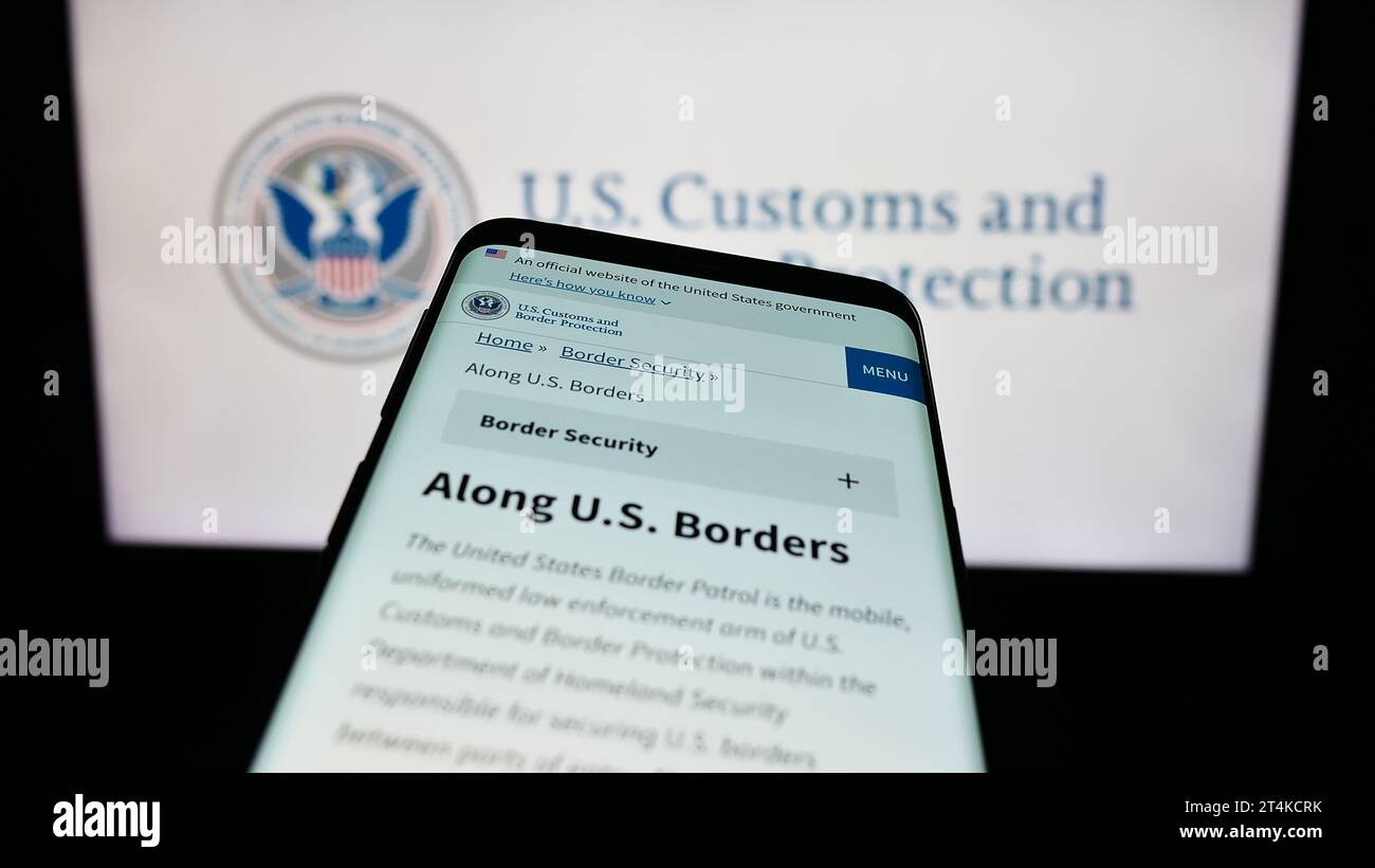 Mobile phone with website of agency United States Customs and Border Protection (CBP) in front of seal. Focus on top-left of phone display. Stock Photo