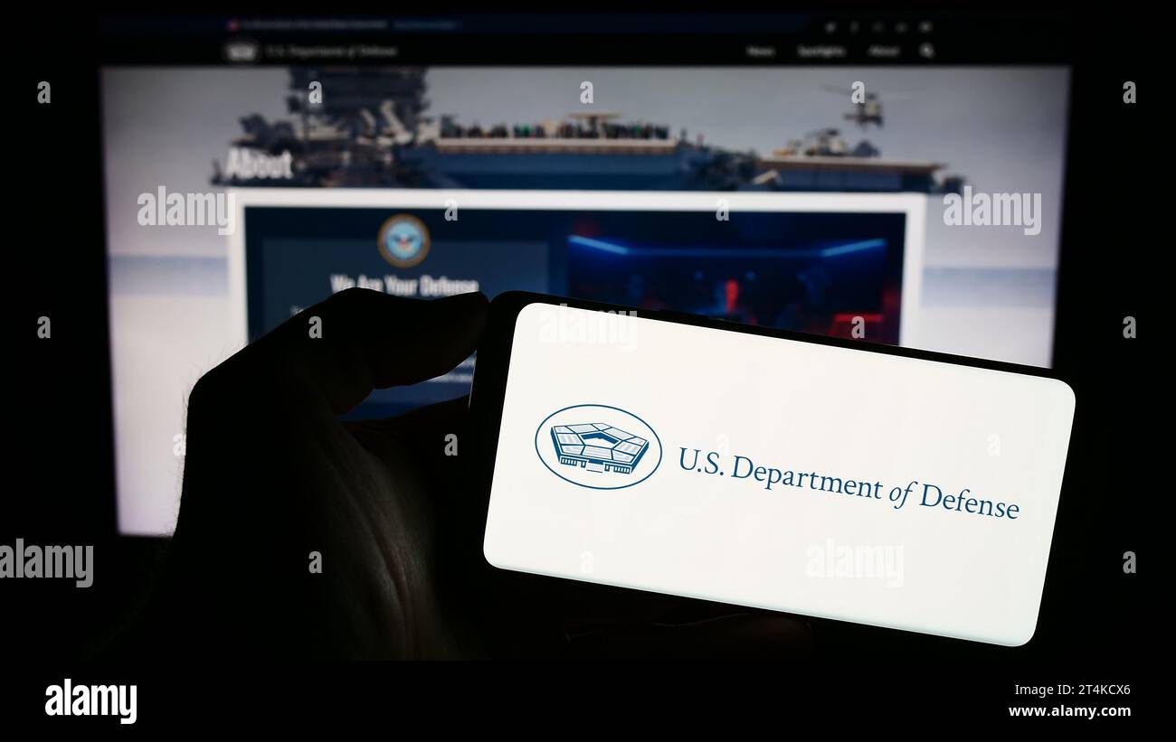 Person holding smartphone with logo of United States Department of Defense (DoD) in front of website. Focus on phone display. Stock Photo