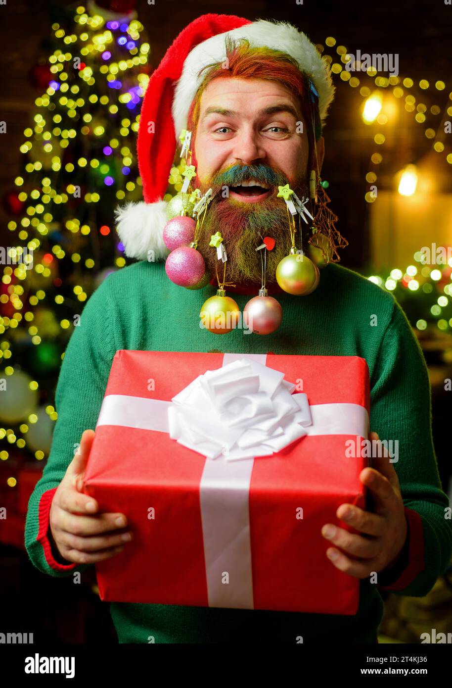 Merry Christmas and Happy New year. Bearded man in Santa hat with decorated beard holds Christmas gift. Santa delivery man with stylish decorated Stock Photo