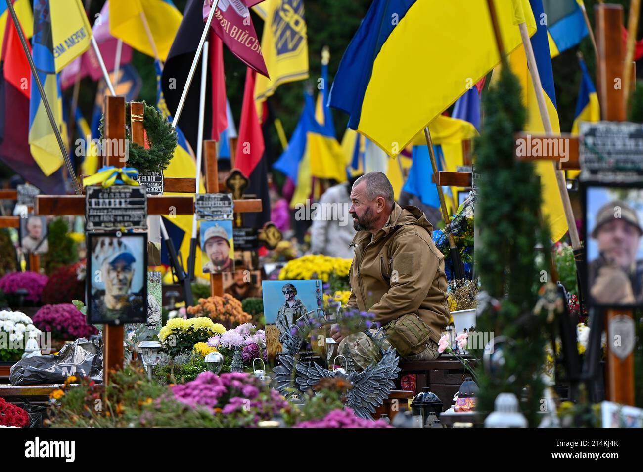 Non Exclusive: LVIV, UKRAINE - OCTOBER 28, 2023 - A man in a camouflage uniform sits by the grave in the field of honorary burials at the Lychakiv Cem Stock Photo