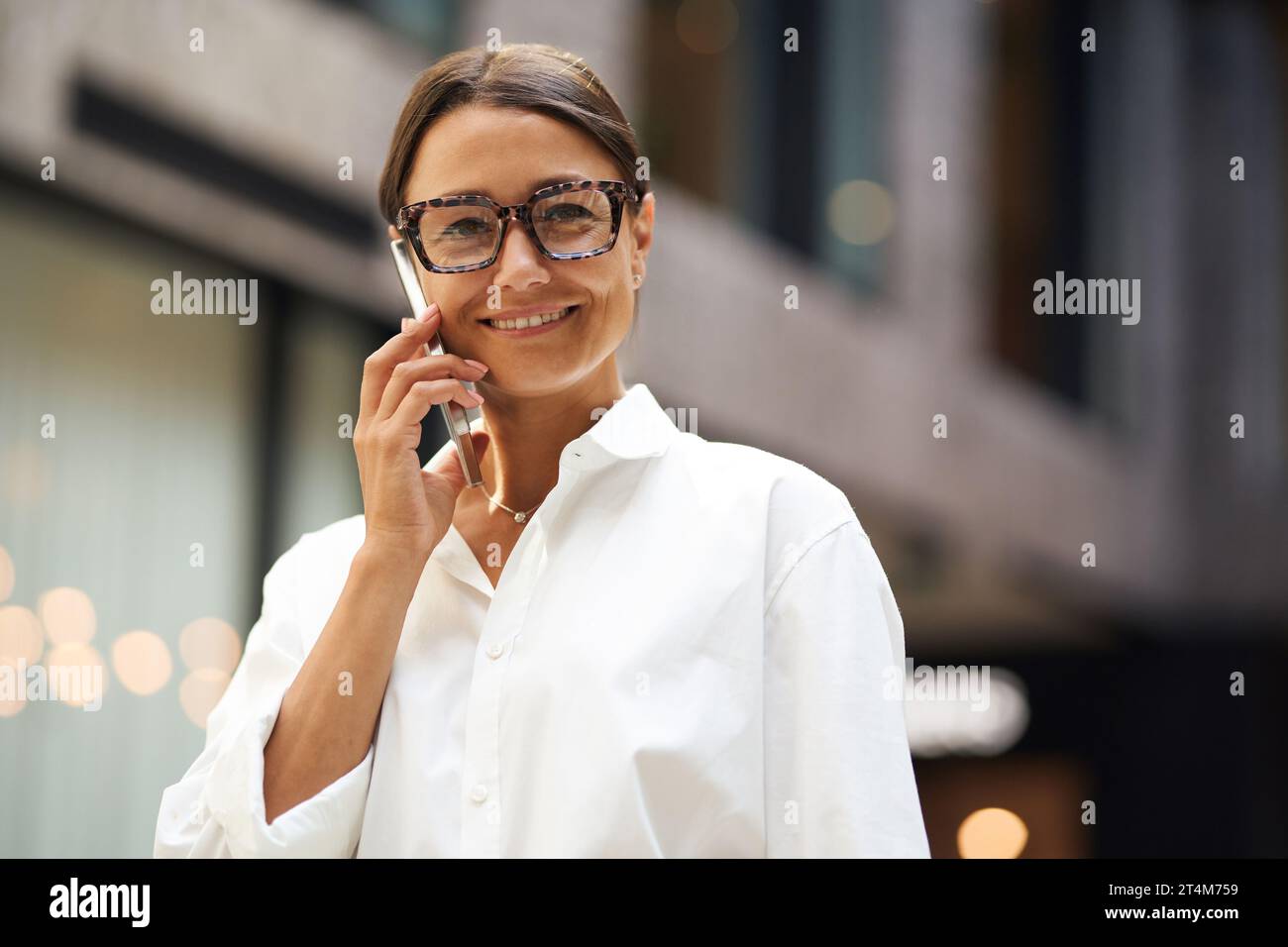 Cheerful woman entrepreneur talking phone with client while standing on office background Stock Photo