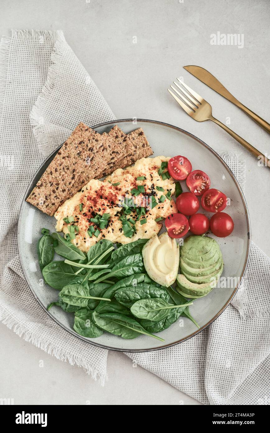 Scramble eggs with cherry tomatoes, fresh spinach leaves, avocado and crispbreads on a plate, top view Stock Photo