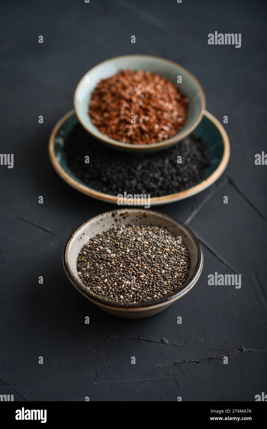 Black sesame, flax and chia seeds in ceramic plates on a dark background Stock Photo