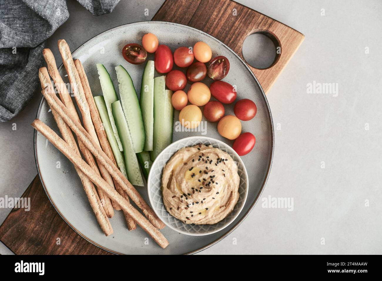 Bowl with hummus, cucumber, cherry tomatoes and grissini breadsticks on a platter on a light background, top view Stock Photo