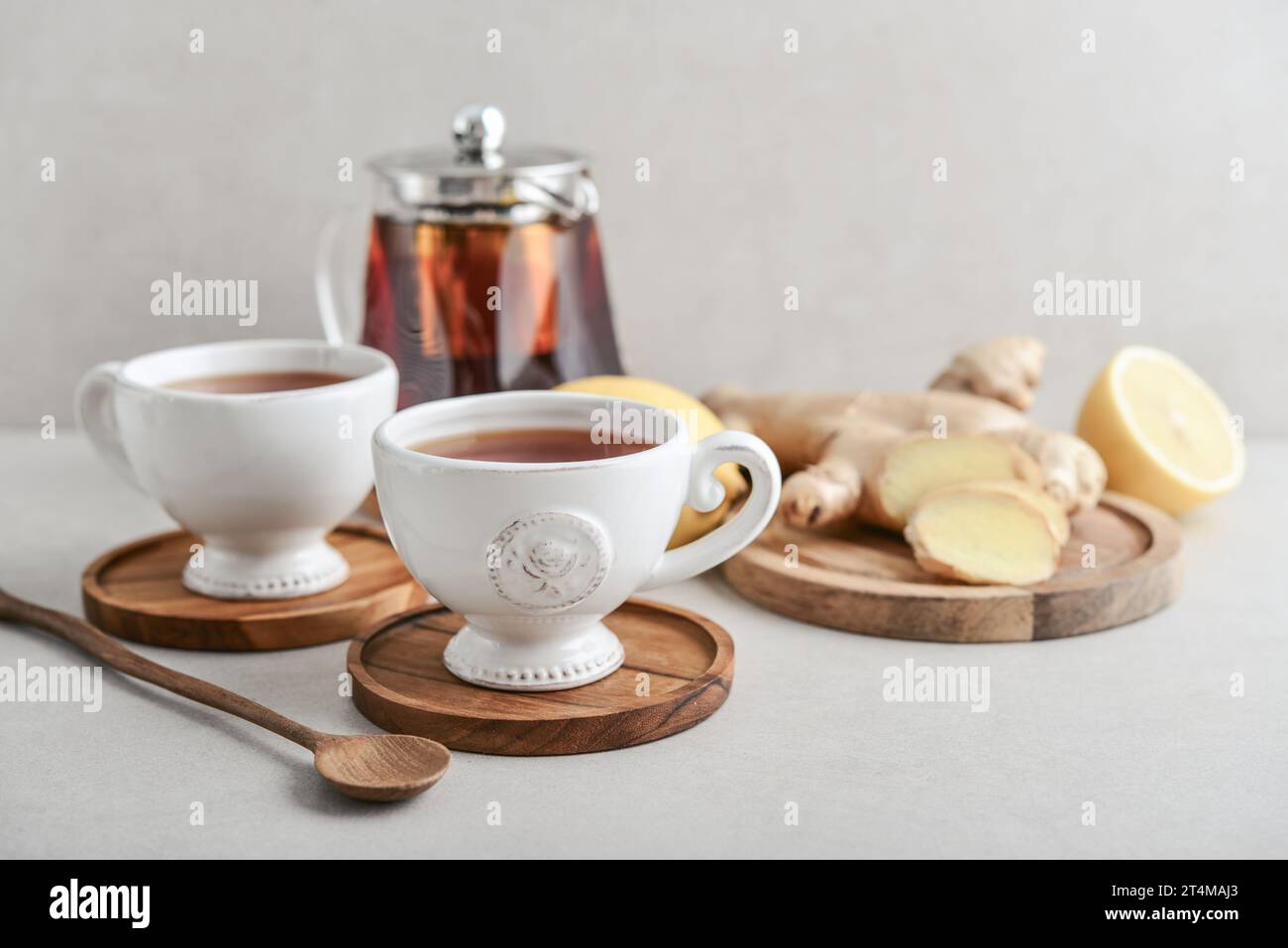 Ginger tea with lemon in a white cups with ginger root  on cutting board and teapot on a light background closeup Stock Photo
