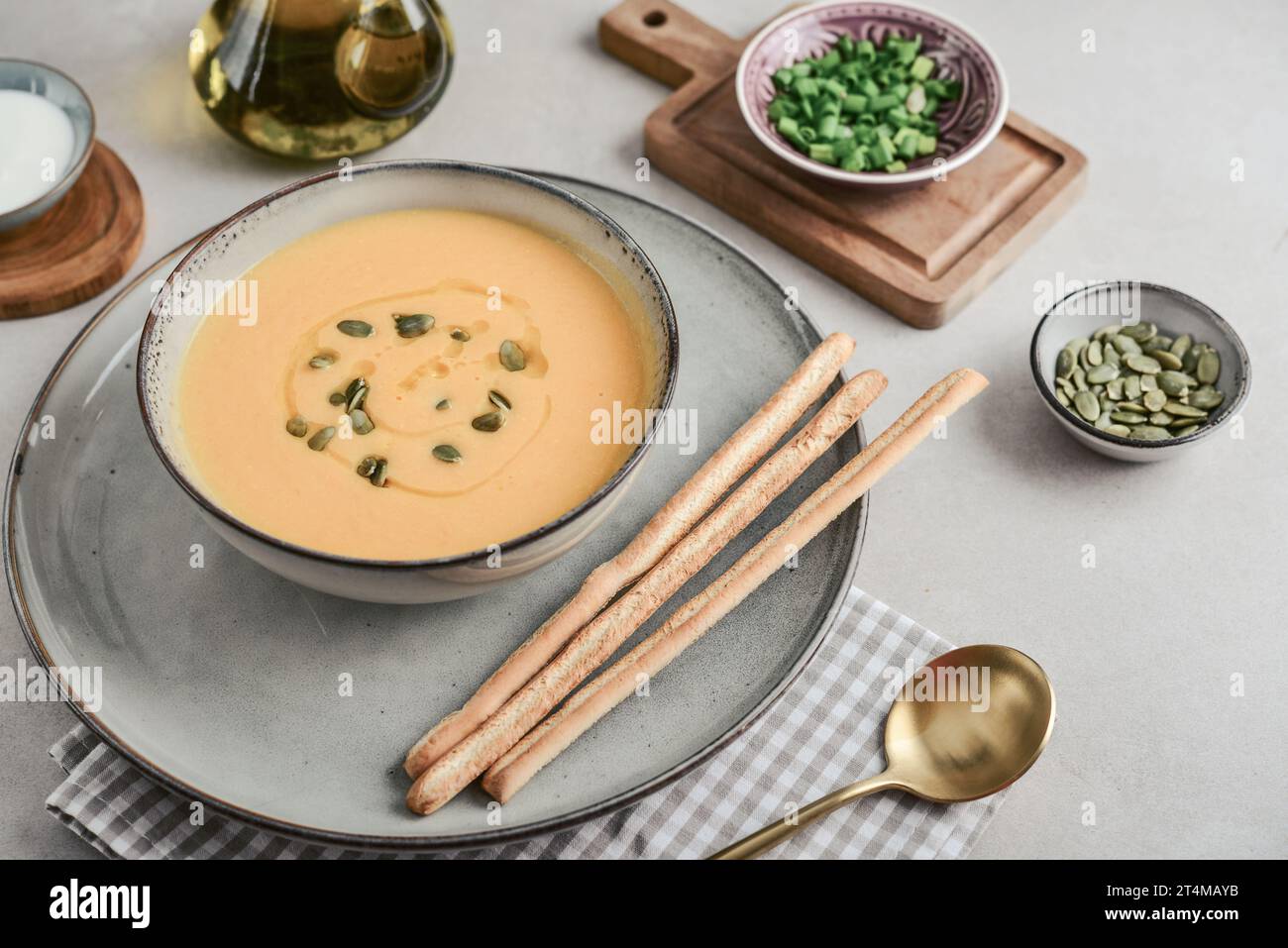 Pumpkin soup in a bowl with pumpkin seeds, green onions and breadsticks on a light background, closeup Stock Photo