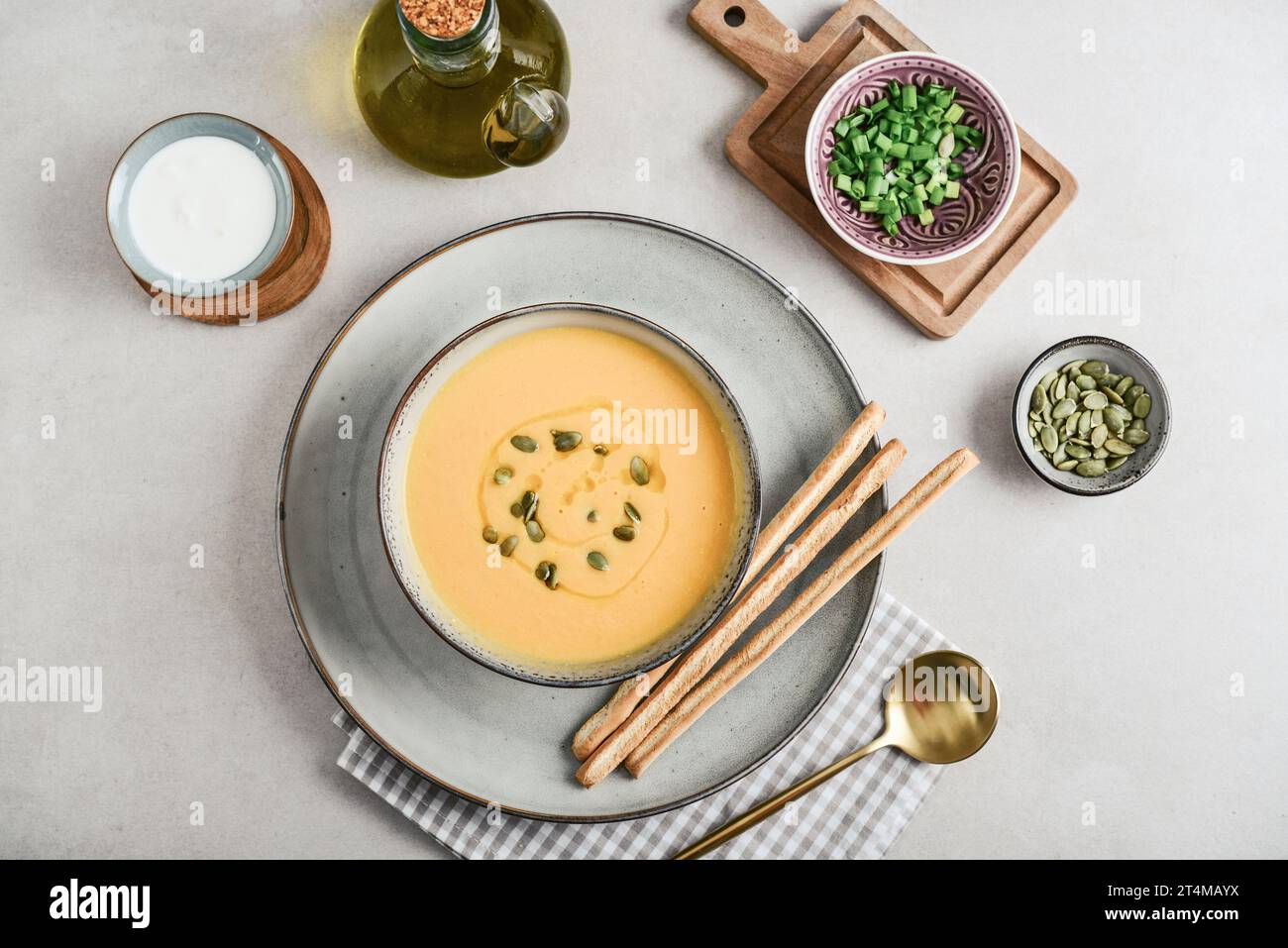 Pumpkin soup in a bowl with pumpkin seeds, green onions and breadsticks on a light background, top view Stock Photo