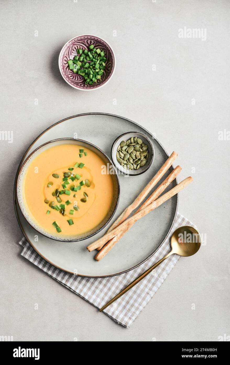 Pumpkin soup in a bowl with pumpkin seeds, green onions and breadsticks on a light background, top view Stock Photo