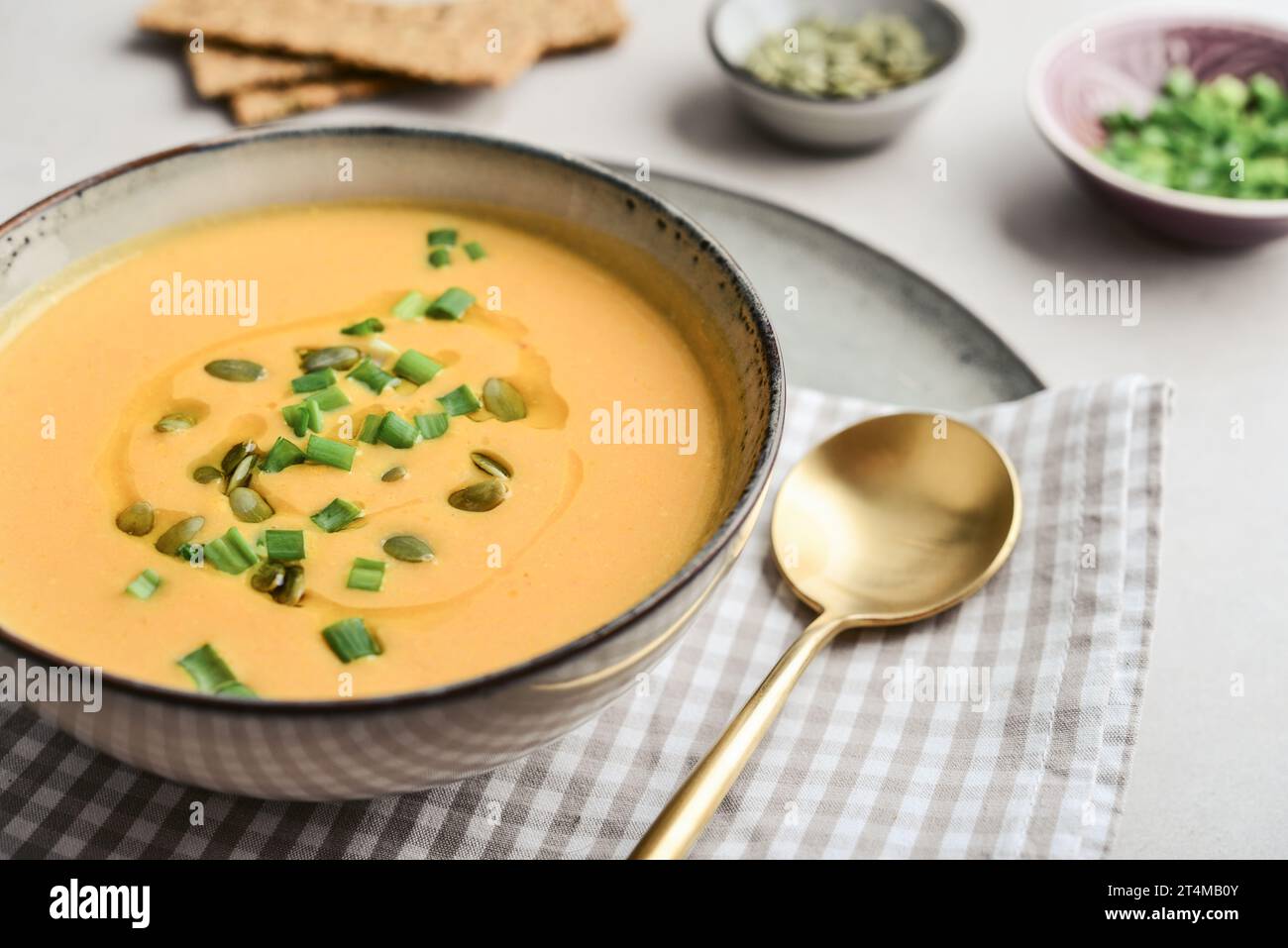 Pumpkin soup in a bowl with pumpkin seeds, green onions and breadsticks on a light background Stock Photo