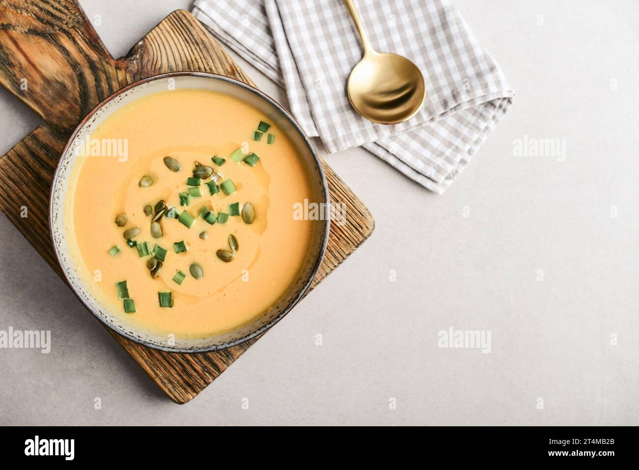 Pumpkin soup in a bowl with pumpkin seeds, green onions and breadsticks on a light background, top view Stock Photo
