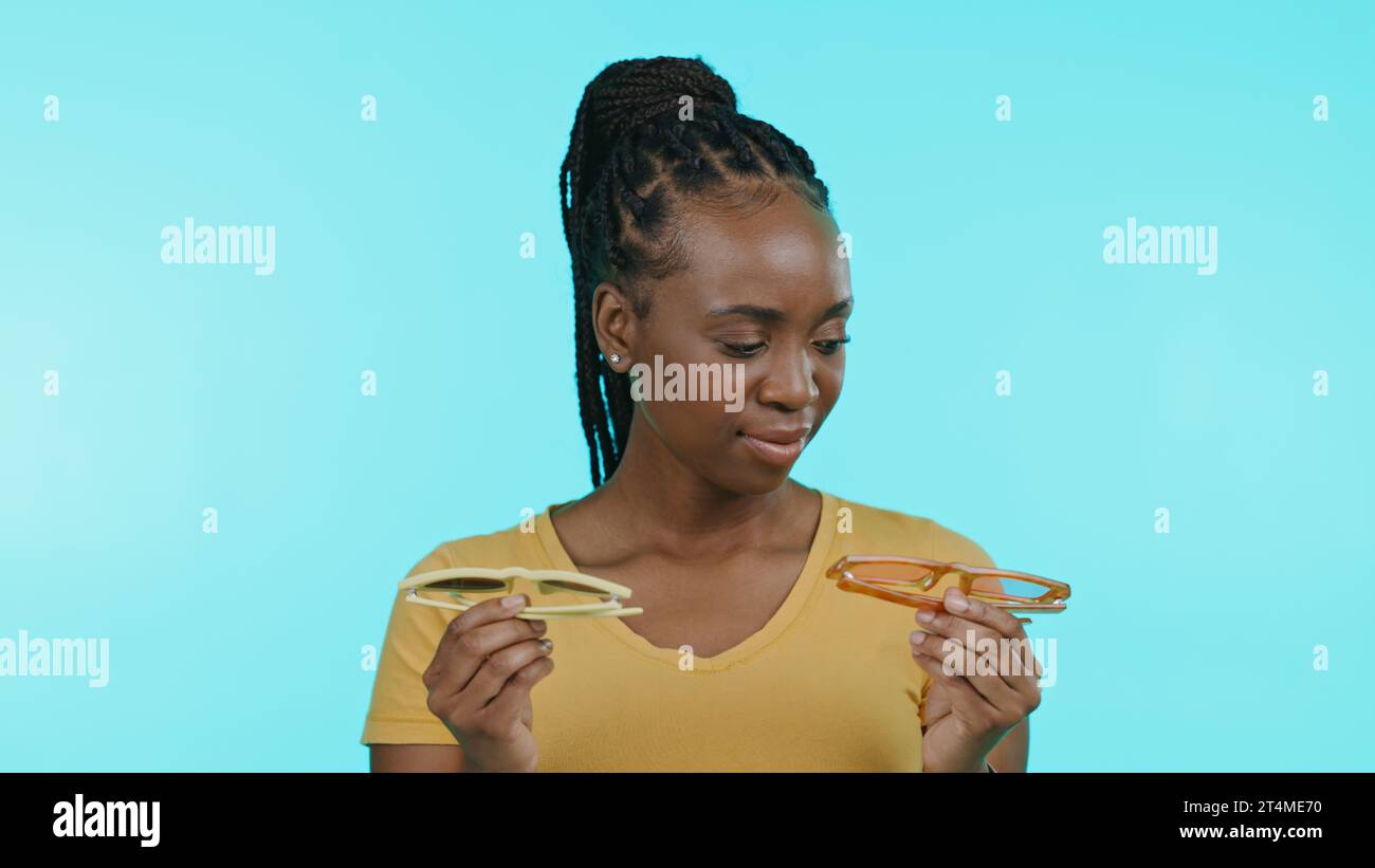 Woman, glasses and fashion choice or decision in studio by blue background, shopping and trendy accessories. Black female model, thinking and choose Stock Photo