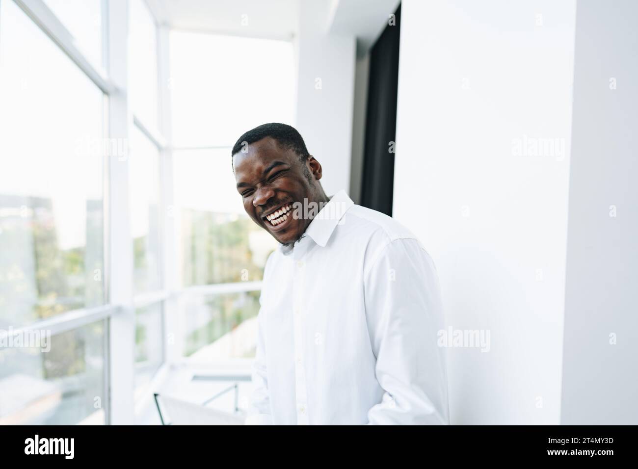 Young african man in white shirt and glasses posing near large window ...