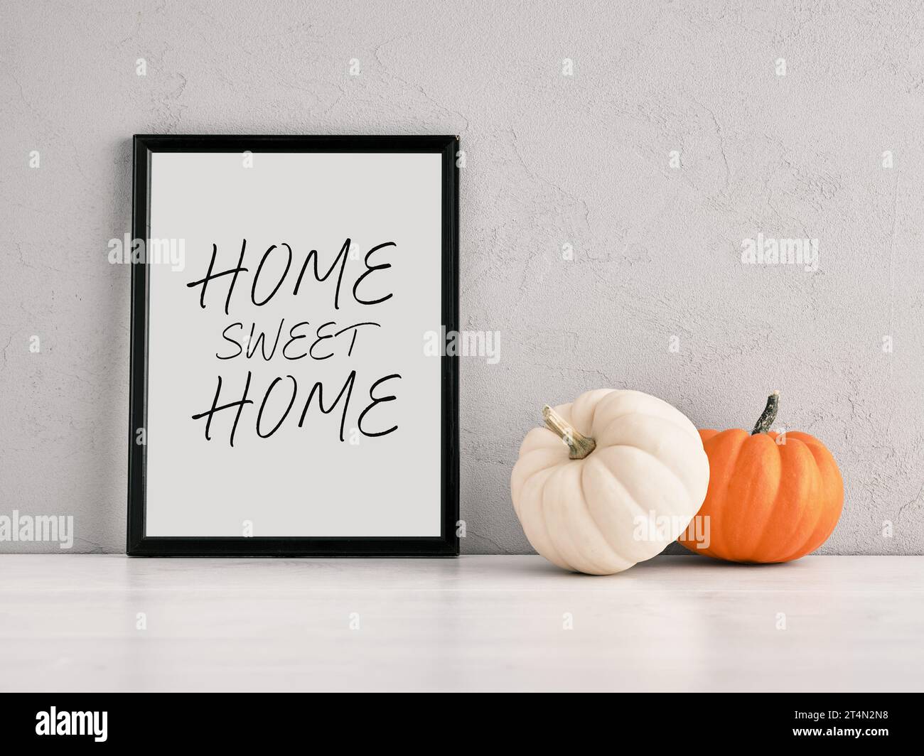 Pumpkins and a frame leaned on a gray wall with the message Home Sweet Home. Stock Photo