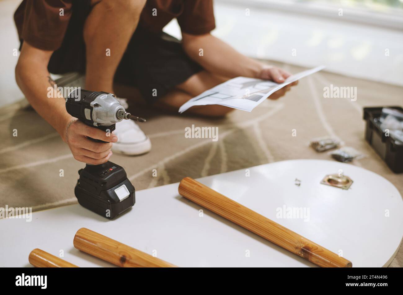 Young man using power drill when when assembling coffee table Stock Photo