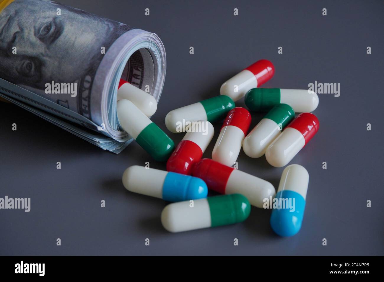 Money rolled up with medicine pills flowing out isolated on black background. Pharmaceutical industry profit, medical expenses concept. Stock Photo