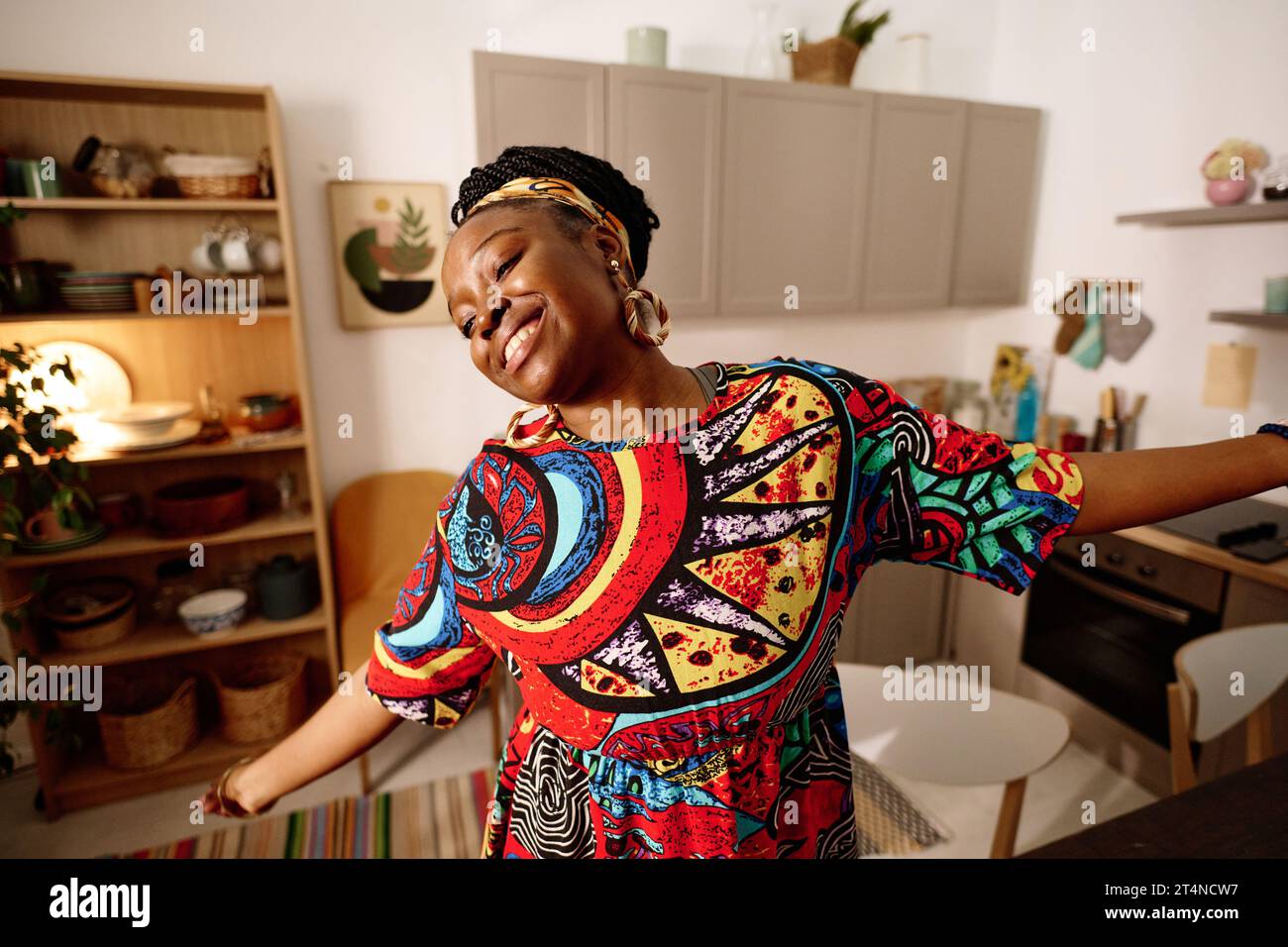 Young ecstatic woman in ethnic dress performing dance in front of camera while celebrating African American holiday in home environment Stock Photo