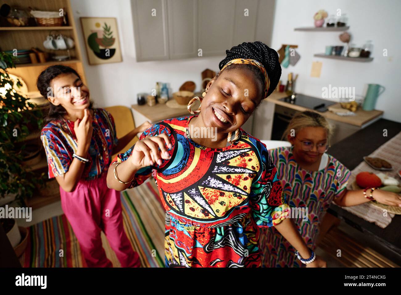 Young cheerful woman in national dress performing dance in front of camera against her two excited daughters dancing with her Stock Photo