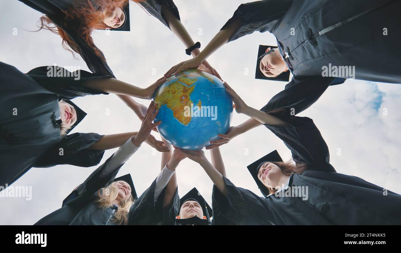 Graduating students embrace a geographical globe of the world. Stock Photo