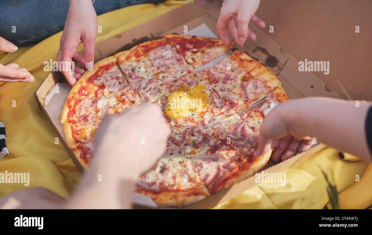 Young students' hands reach for the pizza. Stock Photo