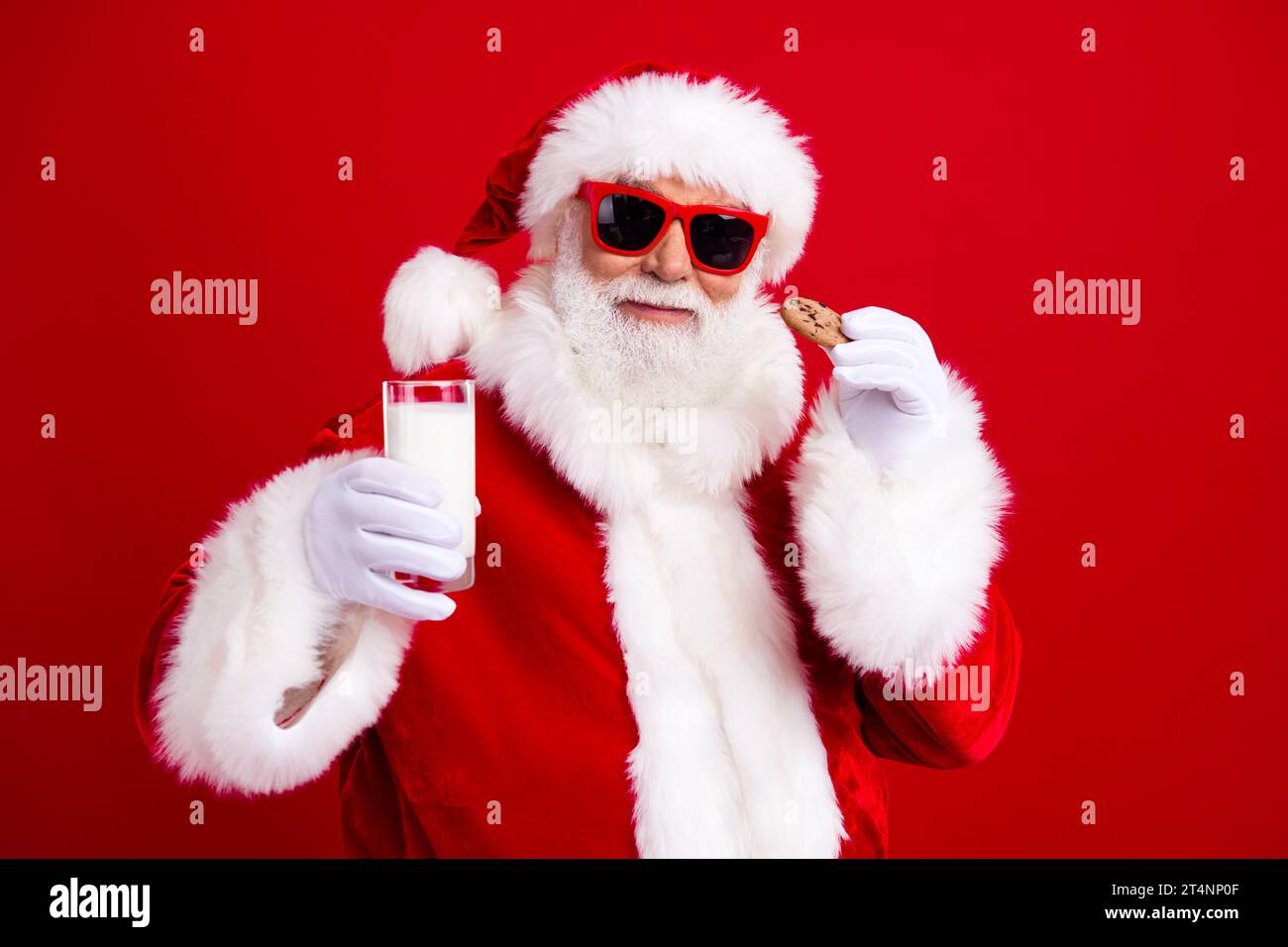 Photo of pleasant grandfather wear stylish santa costume hold glass of milk cookies at christmas eve isolated on red color background Stock Photo