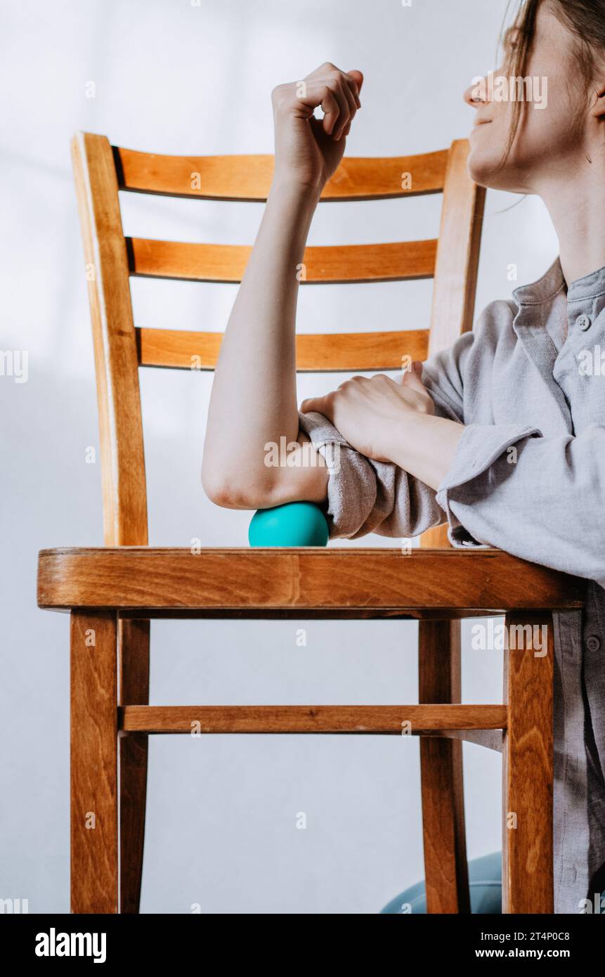 Woman doing triceps massage with therapy ball on wooden chair Stock Photo