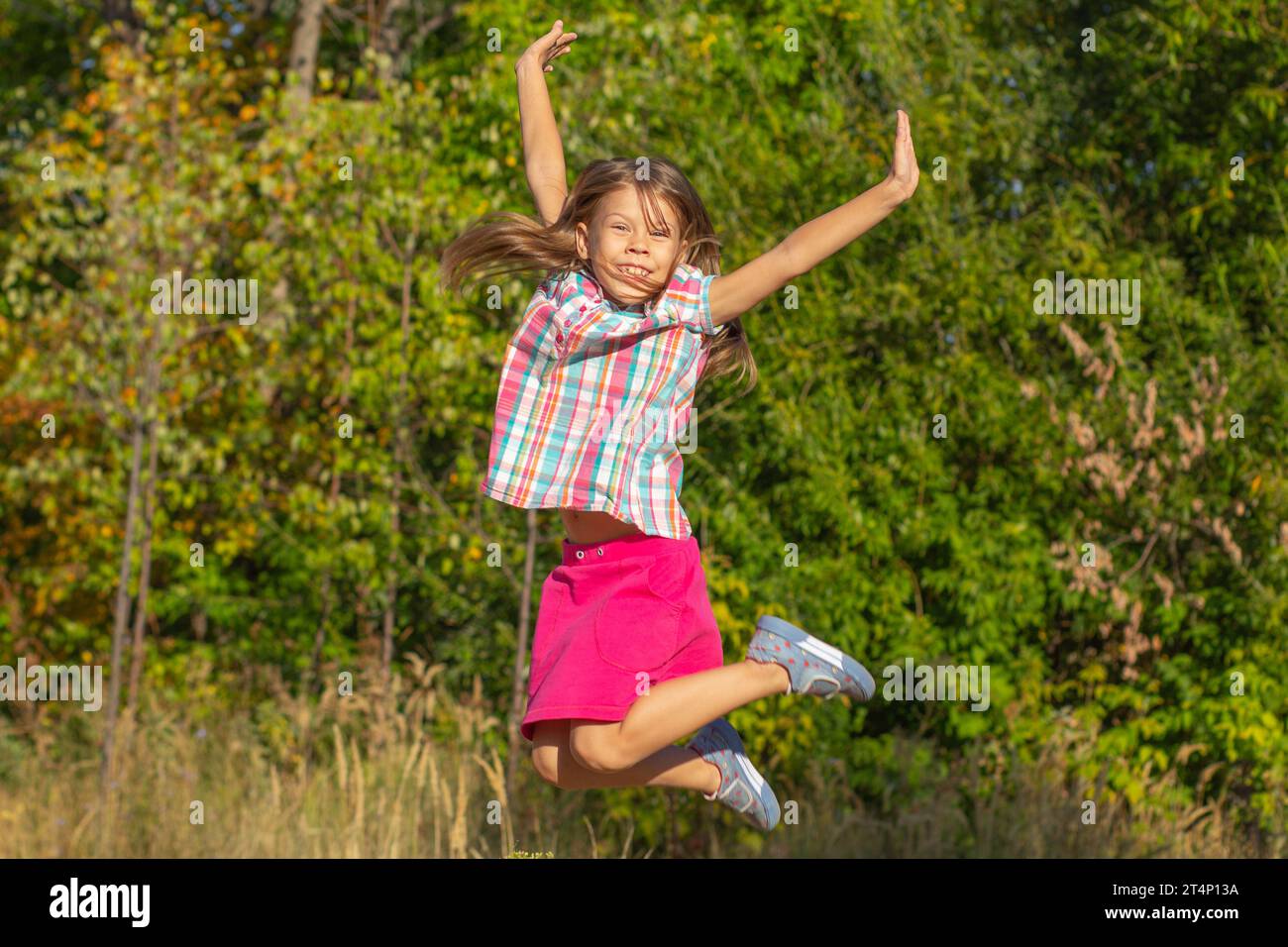 Happy little girl jumping with the raised arms outside in summertime ...