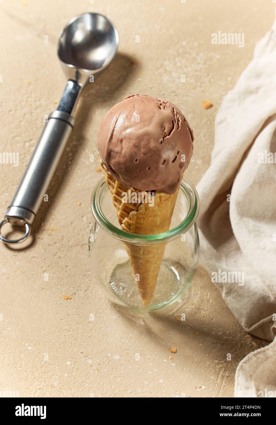 chocolate ice cream in waffle cone and metal scoop on kitchen table ...