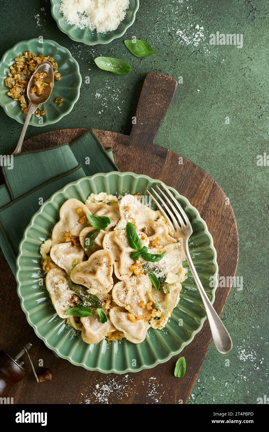 Homemade Italian ravioli pasta in heart shape with beef meat, cheese sauce, caramelized onions, basil and saffron on old green background. Food cookin Stock Photo