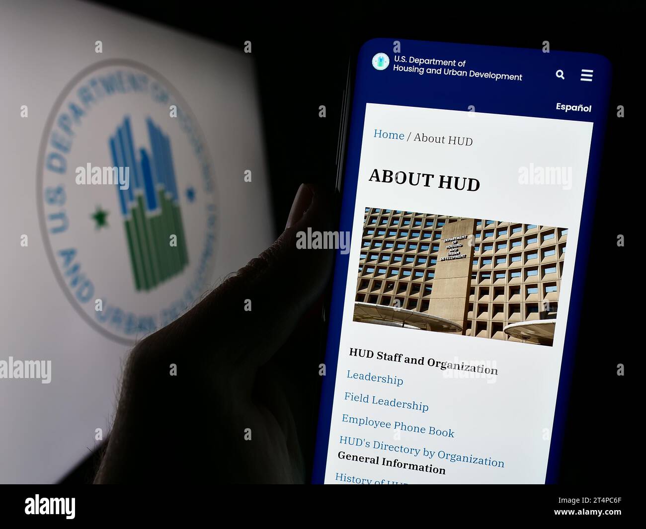 Person holding cellphone with webpage of US Department of Housing and Urban Development (HUD) in front of logo. Focus on center of phone display. Stock Photo