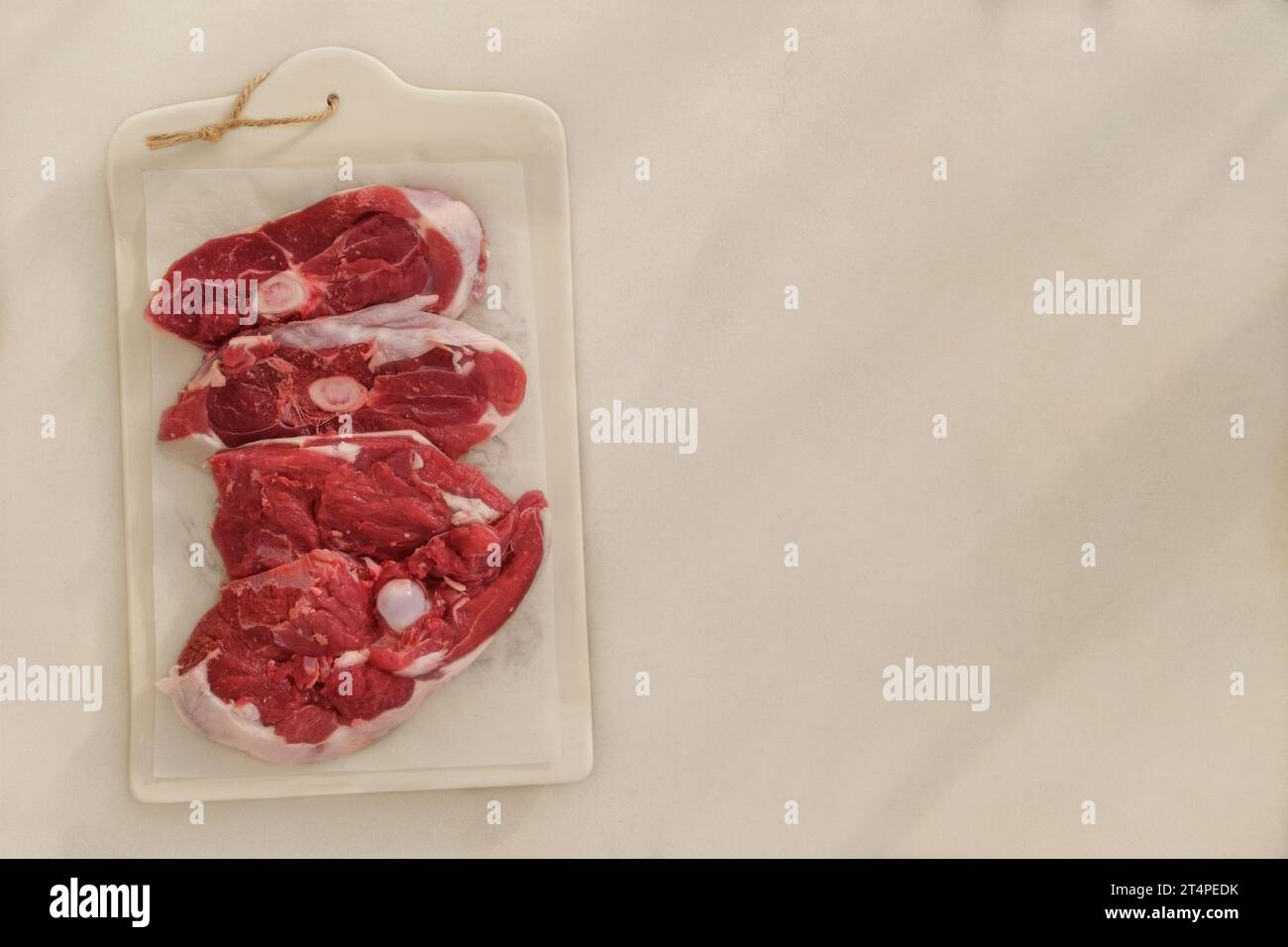 Lamb meat on a ceramic board on beige background. Pieces of meat for cooking. Rear part of the meat carcass. Top view. Stock Photo