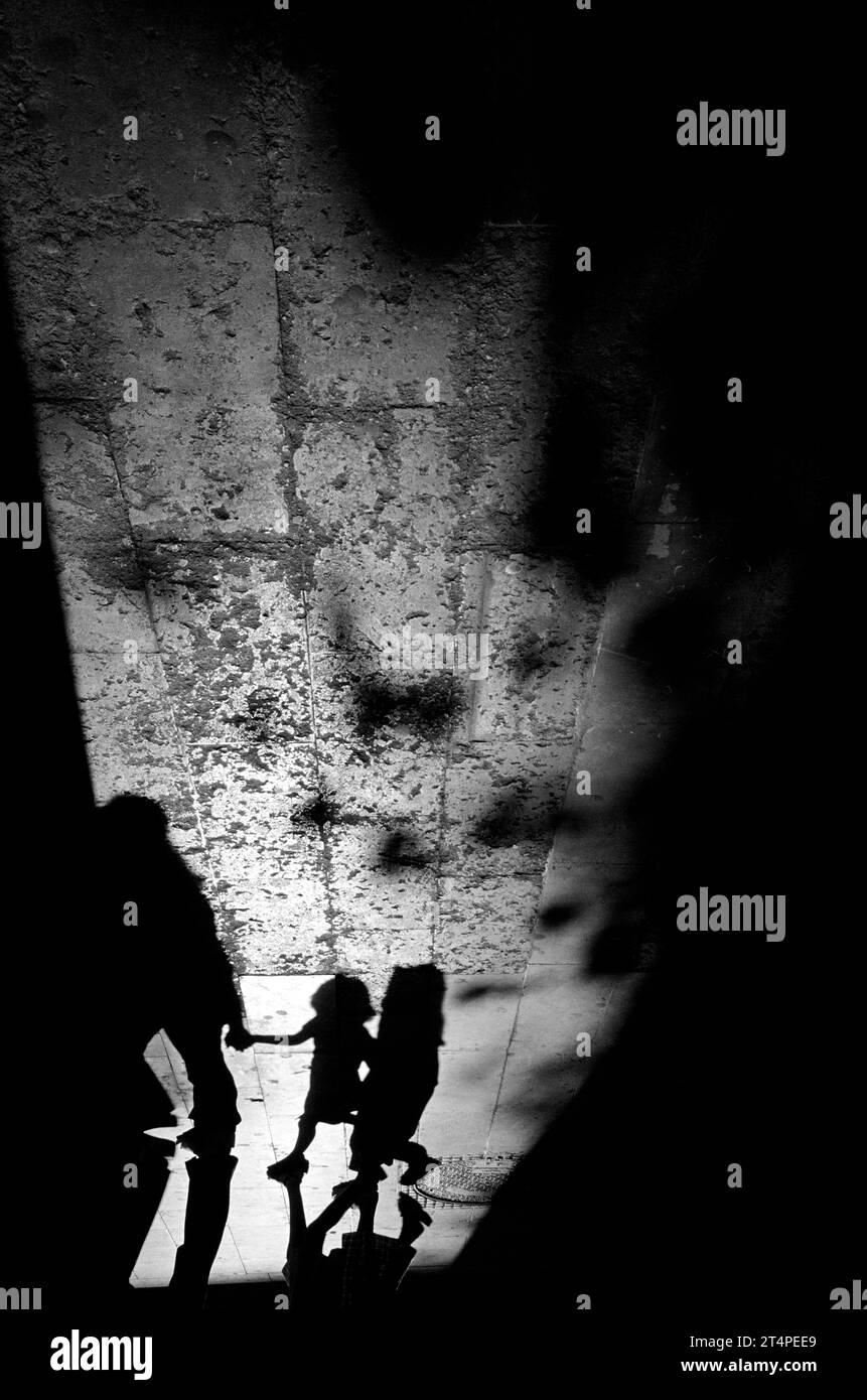 Long dramatic summer evening shadows of family holding hands while walking and tree shadows, cast across old distressed paving stones on Las Ramblas, Barcelona, Spain Stock Photo