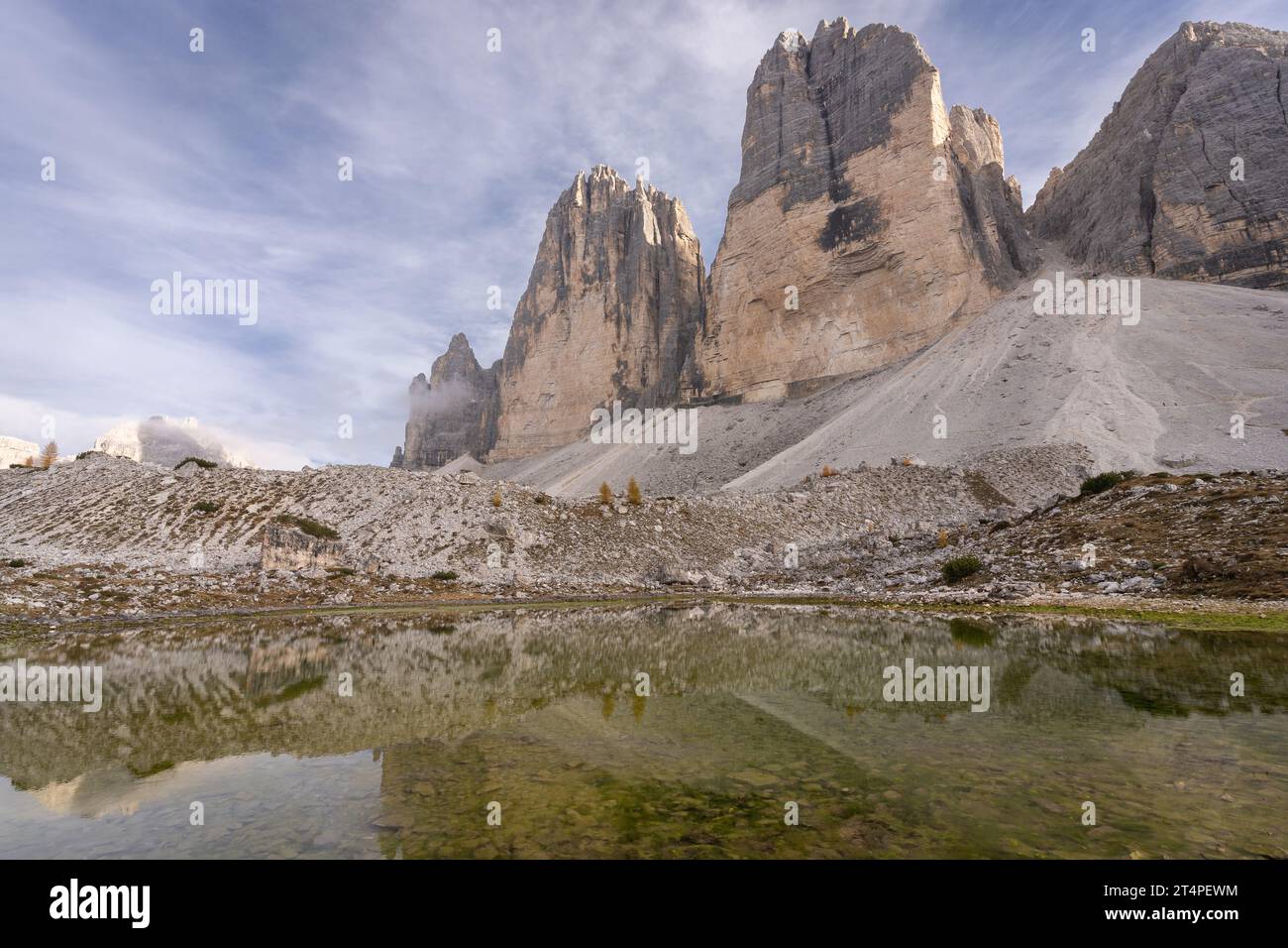 Massive rock formation of Tre Cime reflecting in small pond during autumn day, Dolomites, Italy Stock Photo