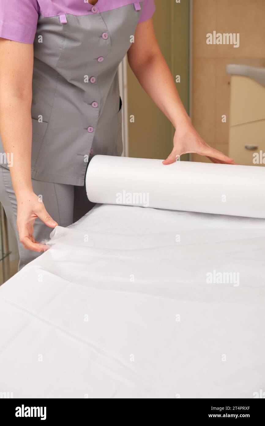 Professional masseuse covering massage table with disposable sheet, preparing to receive patient Stock Photo