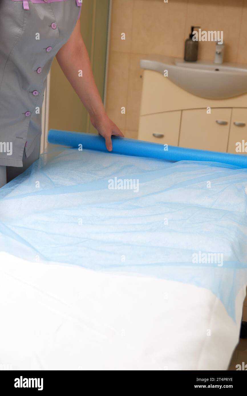 Professional masseuse covering massage table with disposable sheet, preparing to receive patient Stock Photo