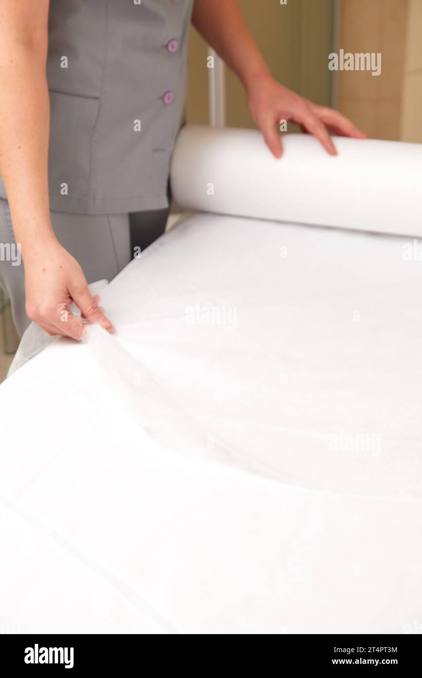 Professional masseuse covering massage table with disposable sheet, preparing to receive patient Stock Photo