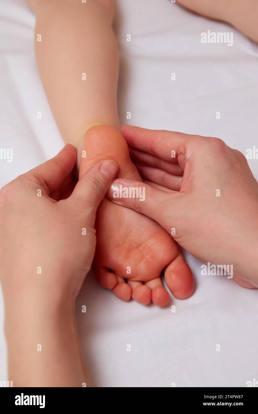 Closeup of small children foot in hands of professional masseuse during reflexology massage. Complementary therapy concept Stock Photo