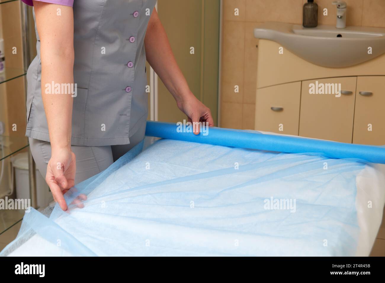 Woman massage therapist preparing equipment to client visit, spreading disposable sheet on massage table. Stock Photo