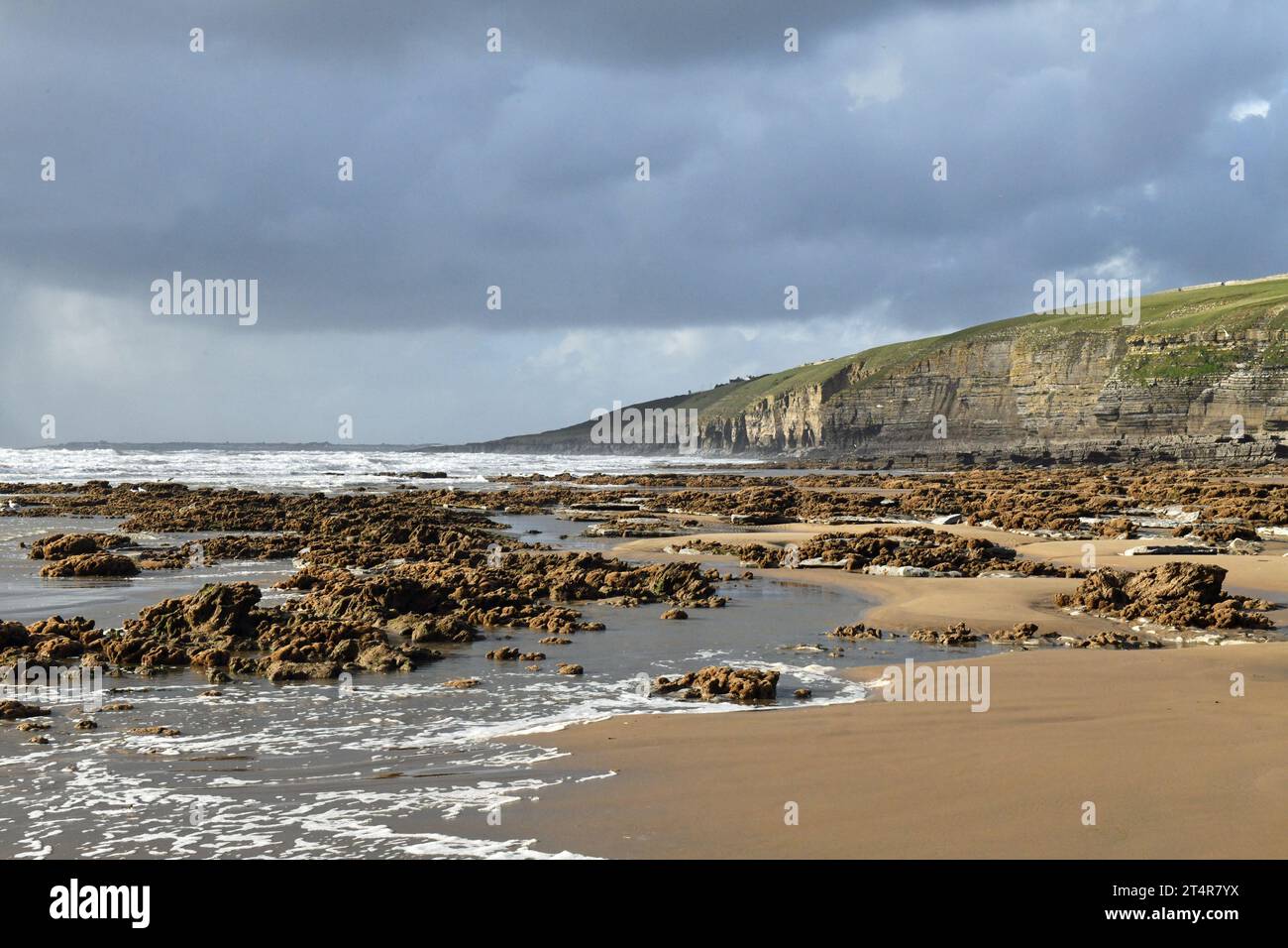 Dunraven Bay with Cliffs behind and rocks and waves and sand infront on a sunny November day on the Glamorgan Heritage Coast in South Wales Stock Photo