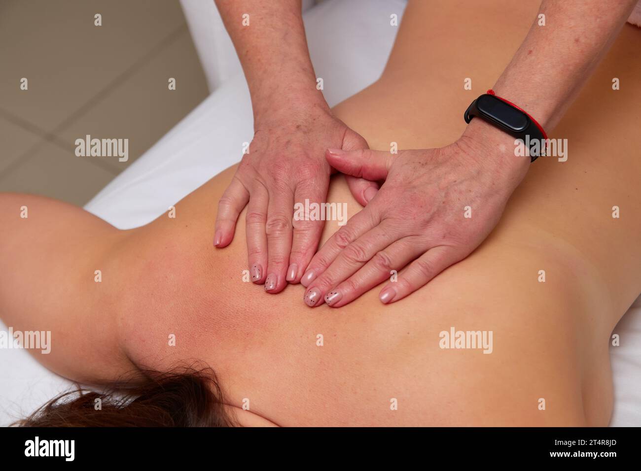 Closeup of skilled masseuse hands giving back pain relief massage to young woman client in medical office Stock Photo