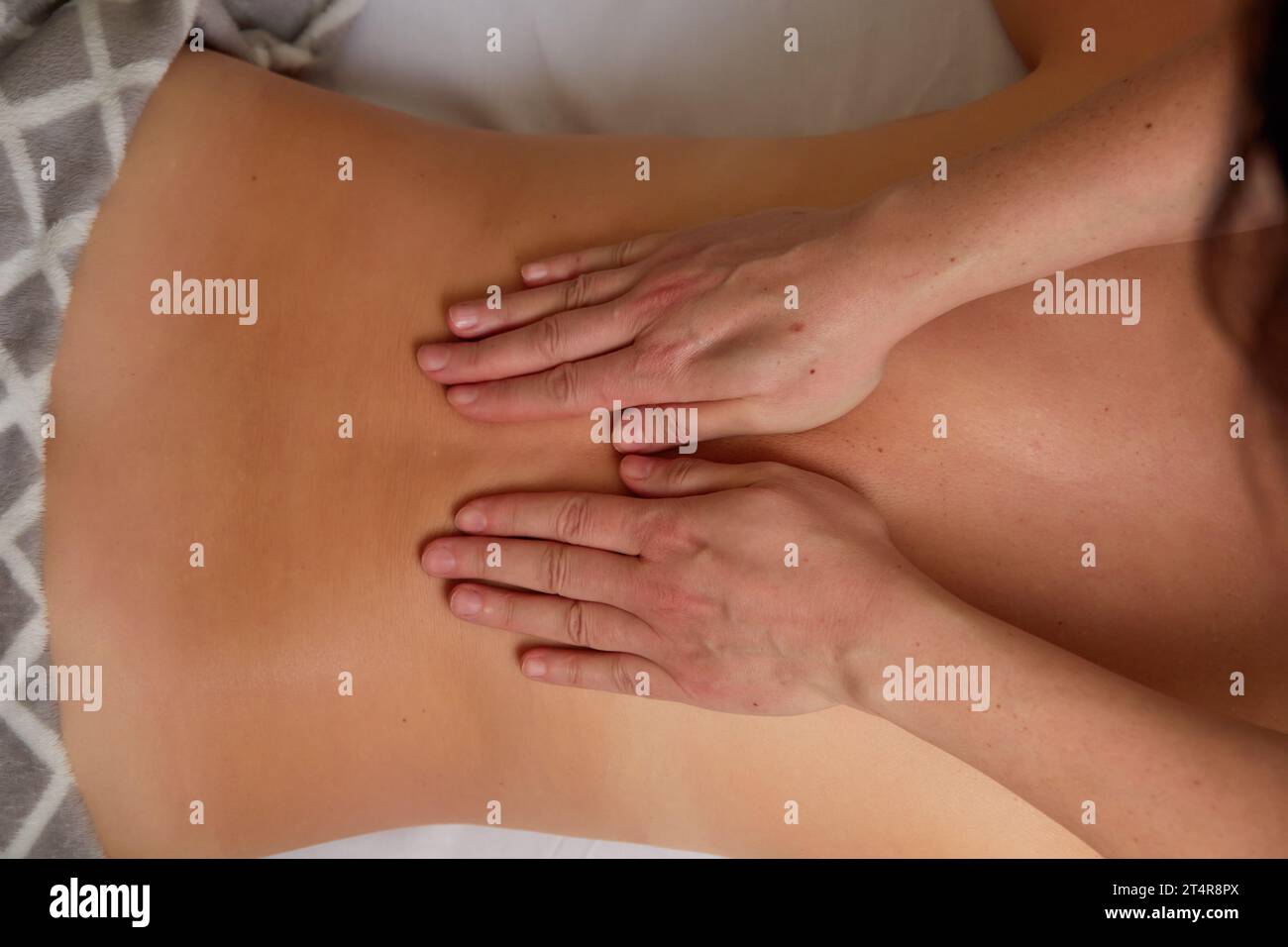 Professional massage therapist making relaxing back massage to young woman in spa salon. Stock Photo