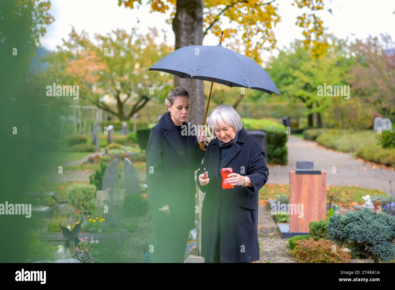 Mother and her daughter-in-law try to light a candle at her son's grave on a cloudy cold day Stock Photo