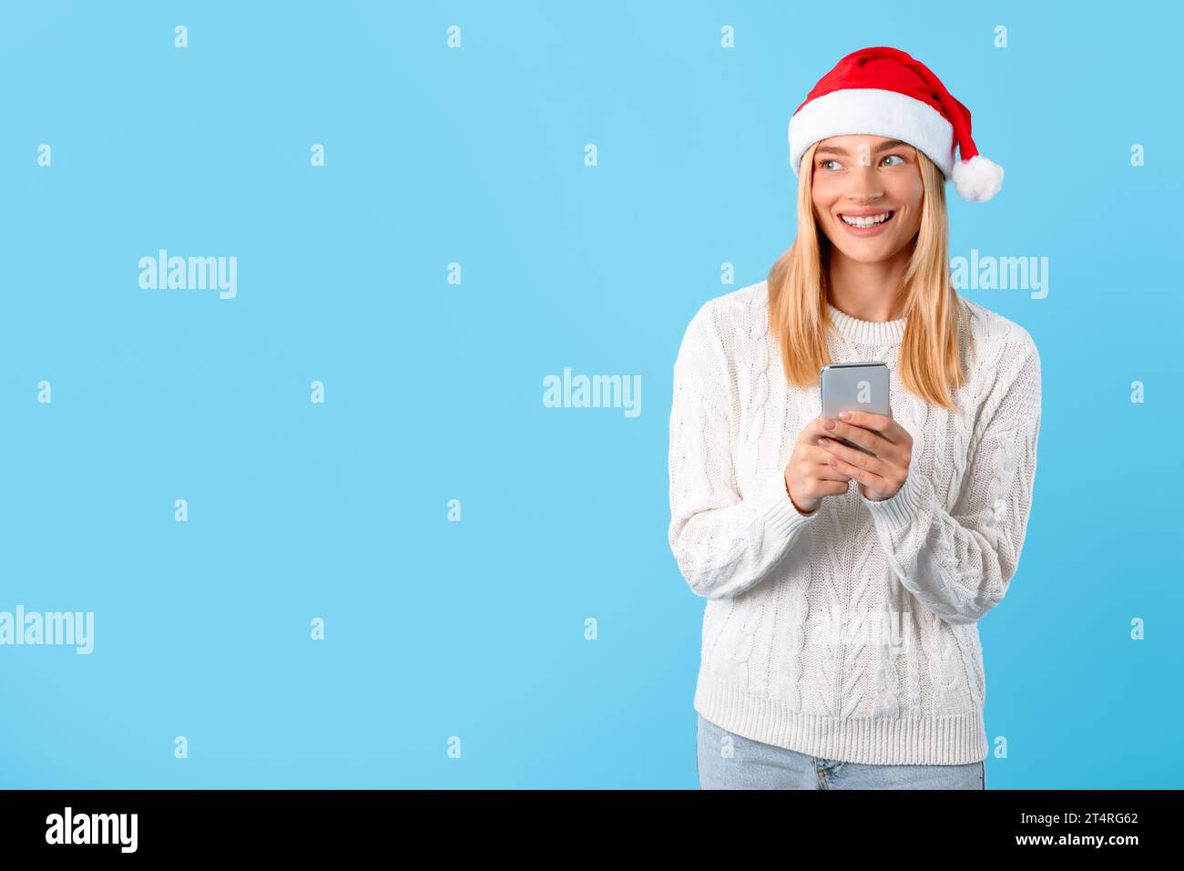 Smiling lady in Santa hat checking Christmas deals on phone, looking at free space Stock Photo