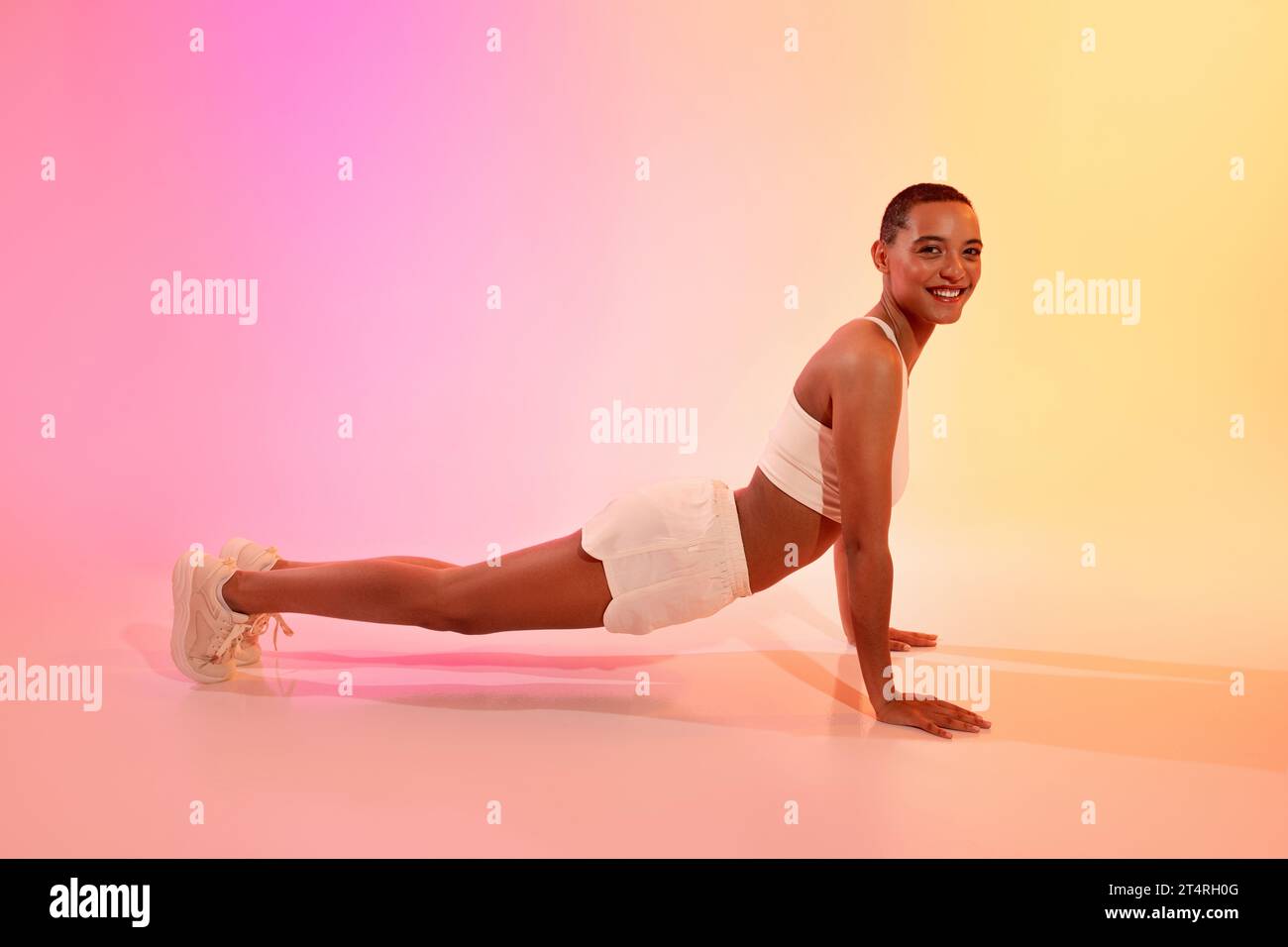 Positive young latin lady in sportswear does push-ups, plank workout on floor Stock Photo