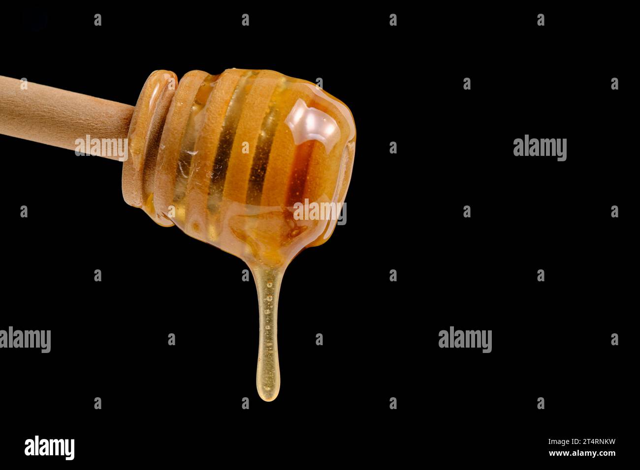 Liquid and fresh honey dripping from wooden honey spoon black background Stock Photo