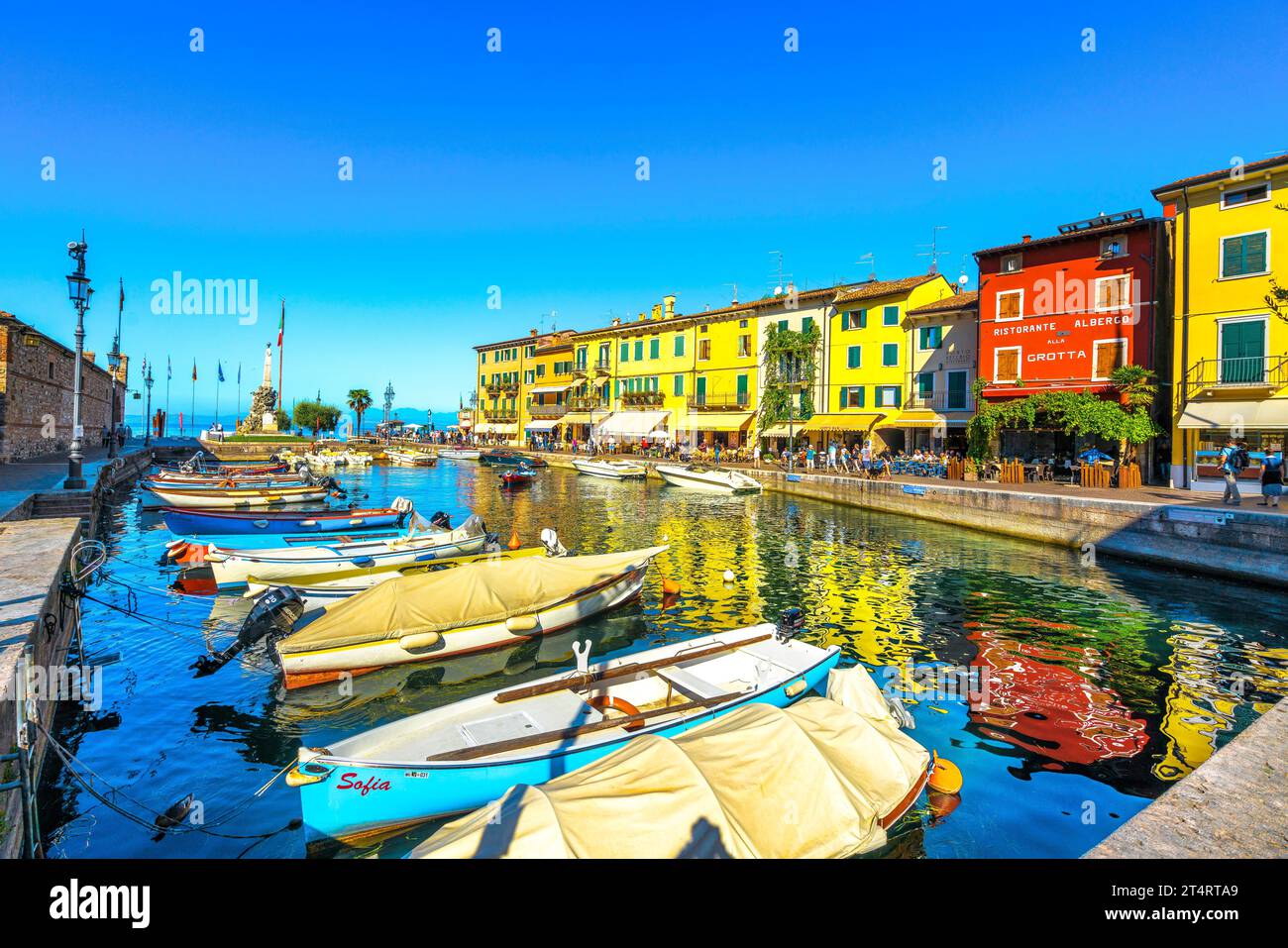 LAZISE, VENETO - ITALY - SEPTEMBER 28, 2018: Boats in old town port of Lazise and tourists walking in the morning. The town is a popular holiday desti Stock Photo